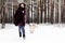 Smiling young woman is running with her South Russian Shepherd Dog on a background of winter forest.