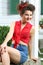 Smiling young woman in shorts sits next to house.