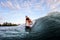 Smiling young woman sit with bent knees on surf style wakeboard and rides on wave