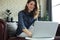 Smiling young woman sitting on sofa with laptop computer and chating with friends