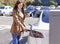 Smiling young woman standing on city parking near electric car, charging automobile battery from small city station