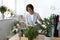 Smiling young woman water green plants in office