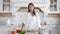 Smiling young woman in white shirt trying slice of fresh organic cucumber while cooking vegan salad