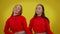 Smiling young women moving simultaneously dancing at yellow background looking at camera. Confident Caucasian twin