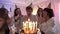 Smiling young women opening eyes of millennial birthday man blowing out candles. Group of Caucasian joyful friends