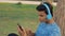 A smiling youngster with a blue headphone checking his mobile in the park
