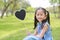 Smilling little Asian girl holding blank heart label lying on green grass at summer garden