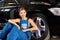 Smilling mechanic girl sits near wheel of black car