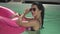 Smilling woman in sunglasses holding pink rubber ring in the water in swimming pool. Leisure of lonely lady in bikini.