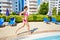 Smling woman in pink sportswear runs along pool