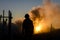 smoke billowing behind silhouette of worker at dawn