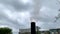 Smoke comes from a black factory chimney against a gray cloudy sky.