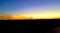 Smoke from a distant fire flows across the horizon against a sunset in the background and a farm field in