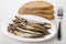 Smoked capelin in oval dish, pieces of bread and fork
