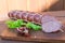 Smoked cutting salami on a old wooden table with green lettuce