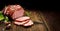 Smoked gammon sliced on a wooden rustic table with addition of fresh aromatic herbs.