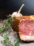 Smoked ham on a stone table with addition of fresh aromatic herbs and spices. Natural product from organic farm, produced by