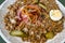 Smoked meat with stewed lentil, pickled cucumber, fried onion and boiled egg on plate, close up