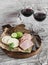 Smoked pork, cheese and two glasses of red wine on a light rustic wood background.