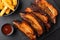 Smoked pork ribs, barbecue sauce and fries in side view on black slate board, top view