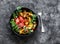 Smoked salmon, baked potatoes, fresh vegetables salad breakfast bowl on a dark background, top view