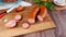 Smoked sausage partially cut into pieces on a cutting board on a wooden background next to knife and vegetables