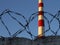 Smokestack against a clear blue sky and a metal barbed wire in front. copyspace for text