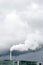 A smokestack emitting white fumes against a stormy sky