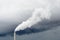 A smokestack emitting white fumes against a stormy sky