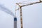 A smoking chimney and a construction crane against a sky