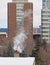 Smoking chimney on a snow covered roof with fir trees and apartment towers behind