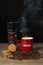 Smoky coffee in red nescafe mug with raw coffee beans, cookies, david off coffee on a table and black background