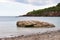 Smooth, calm sea around a shoreline rock at St Mary`s Bay beach in Torbay, Devon, with some coastline cliffs in the background