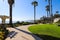 A smooth concreate footpath in the park surrounded by lush green palm trees and plants with green grass and blue sky