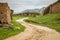 Smooth dirt road winds up a small hill around a mud wall in rural China