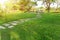 Smooth fresh green grass lawn with random pattern walkway of grey concrete stepping stone in garden of flowering plant