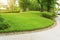 Smooth green grass lawn, trees with supporting and shrub in a good maintenance landscape and garden, gray curve pattern walkway,