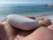 Smooth and round pebble on woman hand palm on summer beach background . Is visible the wedding ring on the hand