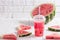 Smoothies Of Watermelon Juice In A Plastic Cup With A Straw. Fresh Red Drink With Ice On The White Background Of Wooden Planks. C