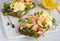 Smorrebrods, open Danish sandwiches with baked salmon, egg salad and microgreens on a white ceramic board against a light concrete