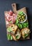 Snack board - prosciutto, olives, grilled mozzarella spinach sandwiches on dark background, top view. Mediterranean style snack, a