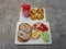 Snack containing bread with meat roll, cheese, tomatoes with cucumber and muffins with melon, all on paper trays