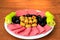 Snack plate on a brown wooden background. Green olives stuffed with peppers, pickled blue grapes, peppers and thinly