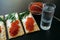 Snack with red caviar and glass of cold vodka on black wooden background. Spirits and traditional starter