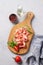 Snack wooden board with bacon or prosciutto on a light background with spices, tomatoes and herbs