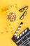 Snacks for film watching. Popcorn and soda near clapperboard, glasses on yellow background top view