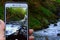 snapshot of waterfall in mountain forest on phone screen that is held in hand on natural background. Carpathian, closeup