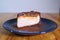 Snickers cheesecake on a blue saucer on a large bright wooden table