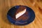 Snickers cheesecake on a blue saucer on a large bright wooden table