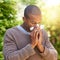 Sniffles, sneezes and wheezes. Shot of a young man blowing his nose outdoors.